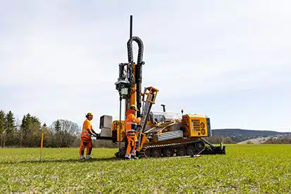 To ansatte med boremaskin ute på et stort gressområde.